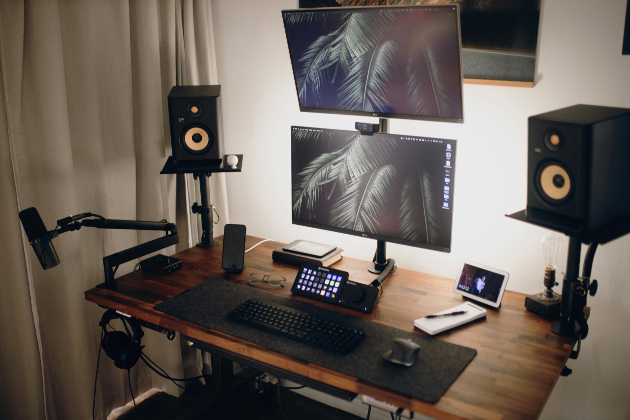 A dual-monitor desk setup with speakers, microphone arm, and recording controls.